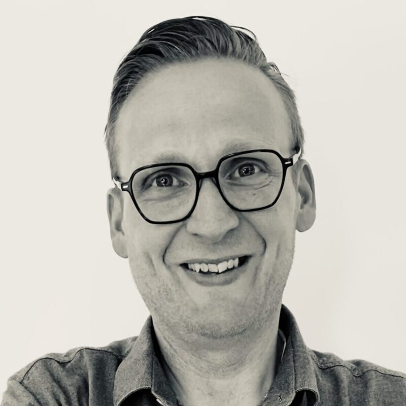 Portretfoto van een man met bril en gekruiste armen, in zwart-wit