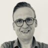 Portretfoto van een man met bril en gekruiste armen, in zwart-wit